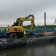 Een graafmachine wordt overgezet naar een sluis eiland voor graafwerkzaamheden